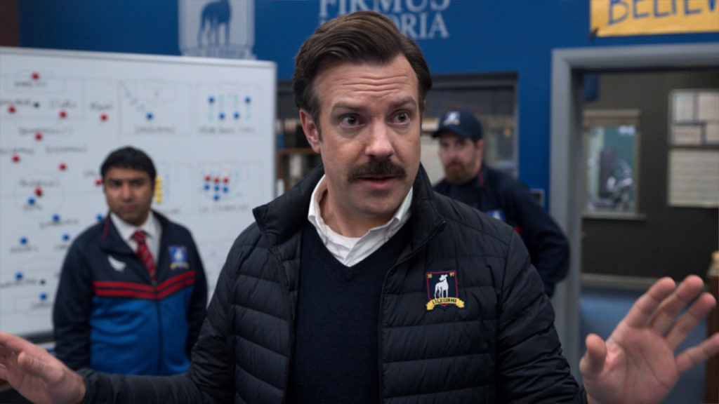 Ted (Jason Sudeskis) gesturing with his hands in the locker room.
