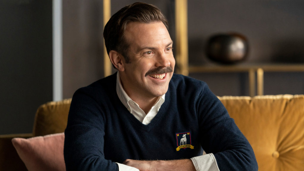 Ted(Jason Sudeikis) smiling on the couch in Hannah's office.